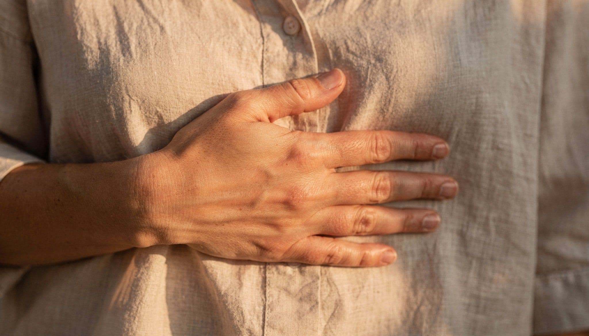 Primer plano de mano de mujer sobre el corazón, luz natural cálida, conexión interior